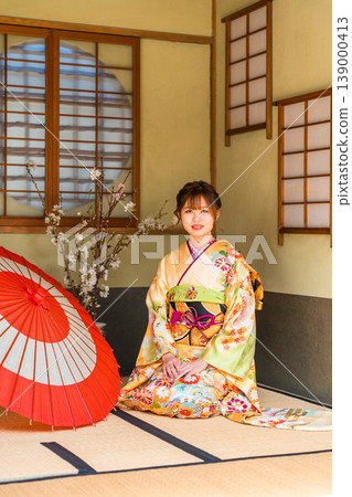 一位穿著振袖和服的日本年輕女子坐在日式房間的榻榻米上（成年禮，20歲生日慶祝活動）。 139000413