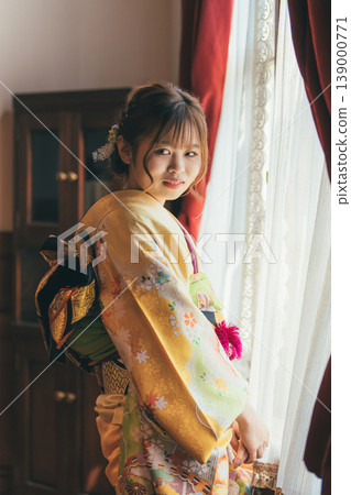 A 20-year-old woman in a furisode kimono gazes out the window of a retro, antique Western-style mansion/studio. A 20-year-old woman in a furisode kimono gazes out the window of a retro, antique Western-style mansion/studio. 139000771