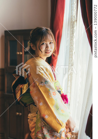 A 20-year-old woman in a furisode kimono gazes out the window of a retro, antique Western-style mansion/studio. A 20-year-old woman in a furisode kimono gazes out the window of a retro, antique Western-style mansion/studio. 139000772