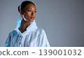 Fashion portrait woman studio white jacket blue light modern style looking away elegant mood, confident female model studio portrait wearing white jacket with blue light accents against gray 139001032
