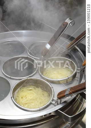 A scene of noodles being boiled in a ramen shop, with steam rising from the machine. 139001218