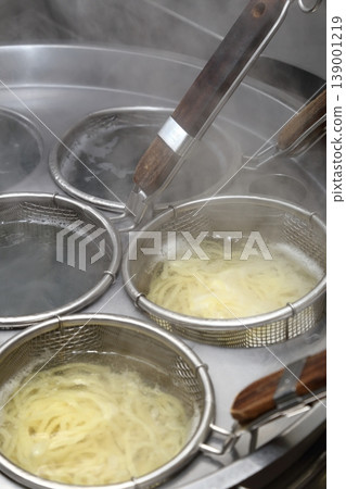 A scene from a ramen shop kitchen showing the process of boiling noodles using a noodle boiling machine. A scene from a ramen shop kitchen showing the process of boiling noodles using a noodle boiling machine. 139001219