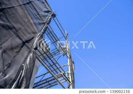 Exterior wall renovation of a detached house: Looking up at the blue sky with scaffolding and protective netting. 139002138