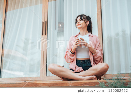 Young woman relaxing on a terrace at home, holding a cup and enjoying a calm moment 139002432