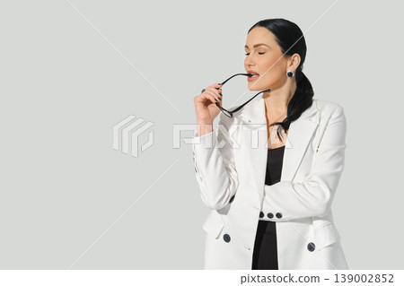 Woman in a white blazer thinking while holding sunglasses in a bright setting Woman in a white blazer thinking while holding sunglasses in a bright setting 139002852