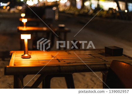 Illuminated table lamp on wooden table at beach restaurant at night Illuminated table lamp on wooden table at beach restaurant at night 139002957
