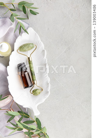 Jade Facial Roller and Essential Oil Bottle on White Dish 139003486