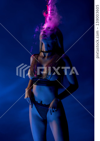 Sensual woman in chainmail lingerie surrounded by pink smoke under blue neon light 139003605