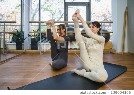 Two women performing advanced yoga stretch holding raised leg. 139004306