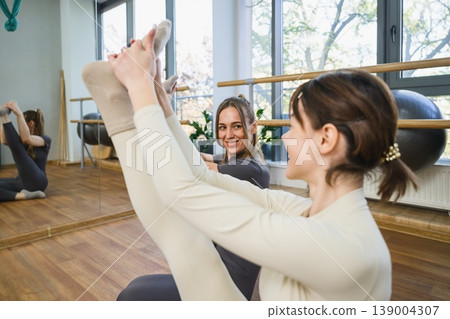 Two women smiling while performing yoga stretch in studio. Two women smiling while performing yoga stretch in studio. 139004307
