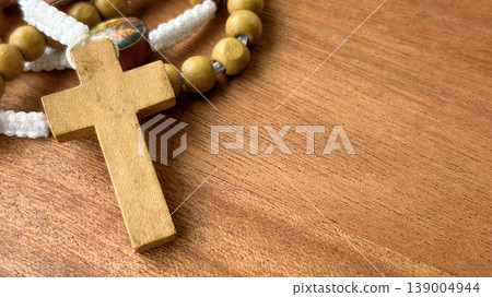 Close view of a wooden cross beside rosary beads on wood symbolizing prayer spirituality and quiet reflection. Close view of a wooden cross beside rosary beads on wood symbolizing prayer spirituality and quiet reflection. 139004944