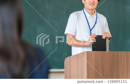 A male teacher teaching in front of a blackboard in a classroom 139005131