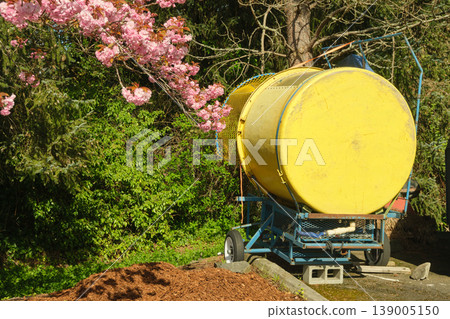 Yellow industrial blower trailer parked near blooming cherry blossoms in spring Yellow industrial blower trailer parked near blooming cherry blossoms in spring 139005150