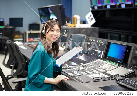 Female broadcast staff working with a smile in the control room of a television station. Female broadcast staff working with a smile in the control room of a television station. 139005235