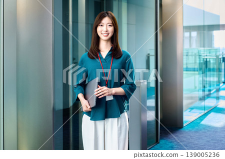 一位面帶微笑的日本女商務人士在辦公室裡拿著筆記型電腦。 一位面帶微笑的日本女商務人士在辦公室裡拿著筆記型電腦。 139005236