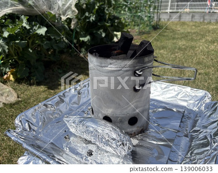 Starting a barbecue fire: Using the chimney effect to ignite the charcoal, using the lawn and fire pit in the garden. Starting a barbecue fire: Using the chimney effect to ignite the charcoal, using the lawn and fire pit in the garden. 139006033
