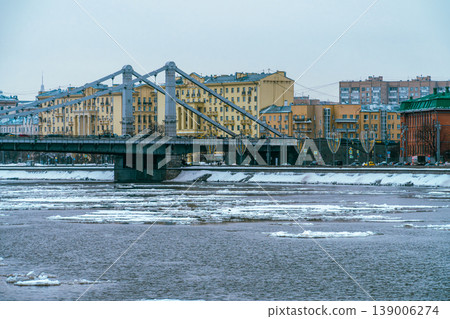 Winter Cityscape With Frozen River and Steel Suspension Bridge Spanning Historic Riverfront Buildings Winter Cityscape With Frozen River and Steel Suspension Bridge Spanning Historic Riverfront Buildings 139006274