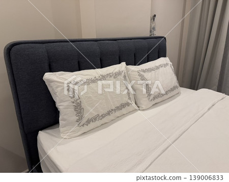 Bed with white pillows and linens in neutral-toned bedroom, suitable for cozy home interior background 139006833