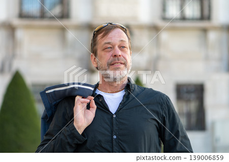 Man about 55 years old holding jacket on shoulder looking aside outdoors 139006859