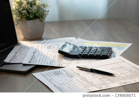 Calculator resting on tax documents with pen and laptop on office desk during financial calculation and document review workflow for accounting, tax filing, expense control, budgeting, and report 139008071