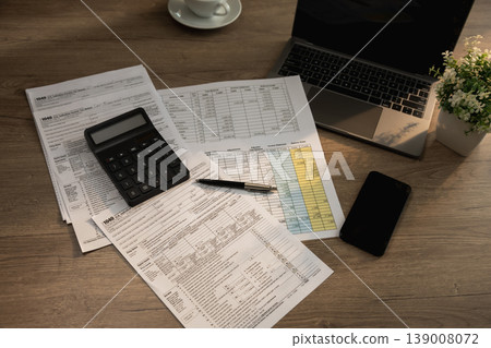 Organized tax filing workspace featuring calculator, laptop, mobile phone, and documents used for accounting preparation, budgeting, expense tracking, financial review, and annual record keeping 139008072