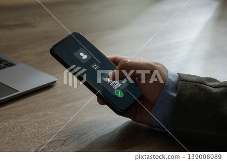 Close-up of a person using a smartphone to confirm a mobile banking transfer payment with a digital interface on a desk next to a laptop, suitable for online payment, fintech, and financial Close-up of a person using a smartphone to confirm a mobile banking transfer payment with a digital interface on a desk next to a laptop, suitable for online payment, fintech, and financial 139008089
