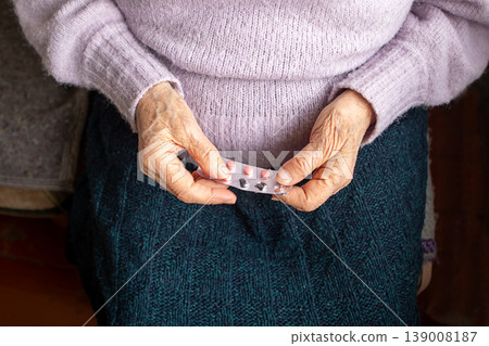 Elderly woman holding blister pack of pills on lap wearing knitted sweater and skirt Elderly woman holding blister pack of pills on lap wearing knitted sweater and skirt 139008187