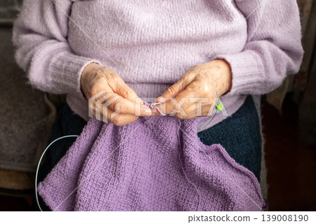 Elderly woman knitting a purple sweater by hand, close-up of caring hands and yarn Elderly woman knitting a purple sweater by hand, close-up of caring hands and yarn 139008190