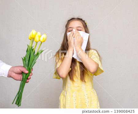Young girl sneezing into tissue while offered yellow tulip flower during allergy season Young girl sneezing into tissue while offered yellow tulip flower during allergy season 139008425