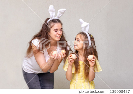 Mother and daughter wearing bunny ears holding Easter eggs and sharing a joyful spring moment Mother and daughter wearing bunny ears holding Easter eggs and sharing a joyful spring moment 139008427