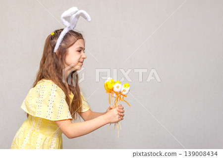 Young girl in yellow dress wearing bunny ears holding decorated Easter eggs Young girl in yellow dress wearing bunny ears holding decorated Easter eggs 139008434