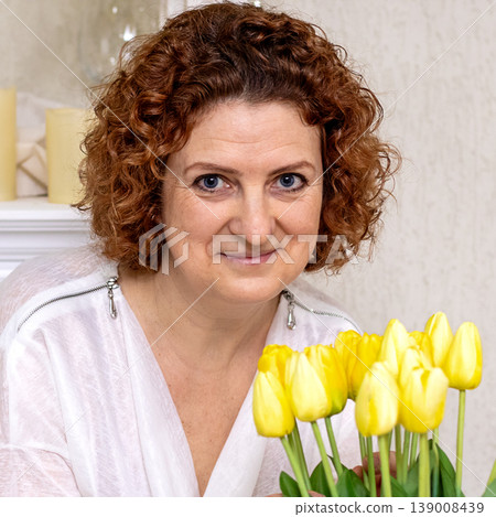 Smiling middle-aged woman holding yellow tulips in a warm home portrait with natural light Smiling middle-aged woman holding yellow tulips in a warm home portrait with natural light 139008439