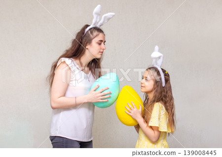 Mother and daughter wearing bunny ears sharing large colorful Easter eggs and playful spring moments Mother and daughter wearing bunny ears sharing large colorful Easter eggs and playful spring moments 139008445