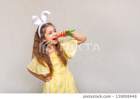 Girl in yellow dress wearing bunny ears playfully biting a carrot with Easter joy Girl in yellow dress wearing bunny ears playfully biting a carrot with Easter joy 139008448