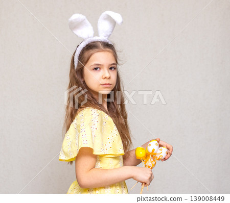 Young girl wearing bunny ears in yellow dress holding decorated Easter eggs Young girl wearing bunny ears in yellow dress holding decorated Easter eggs 139008449