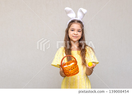 Girl with bunny ears holding an Easter basket and a yellow egg in a summer dress Girl with bunny ears holding an Easter basket and a yellow egg in a summer dress 139008454