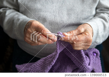 Elderly hand crocheting a purple blanket by hand showing patience, skill and homemade comfort Elderly hand crocheting a purple blanket by hand showing patience, skill and homemade comfort 139008513