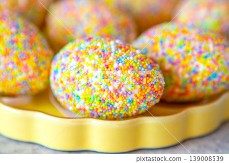 Colorful sprinkle-covered Easter egg on a yellow plate for playful spring celebration and sweet treat Colorful sprinkle-covered Easter egg on a yellow plate for playful spring celebration and sweet treat 139008539