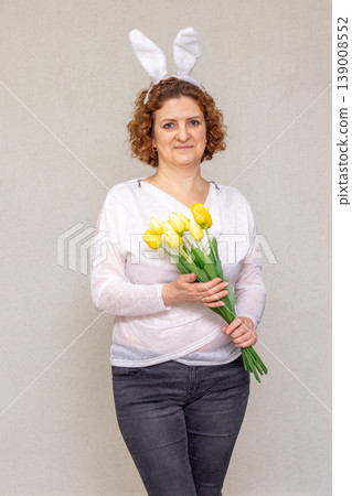 Woman wearing bunny ears holding yellow tulip bouquet in spring portrait for Easter celebration Woman wearing bunny ears holding yellow tulip bouquet in spring portrait for Easter celebration 139008552
