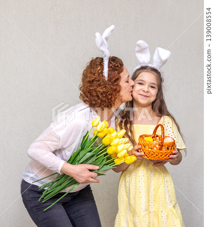 Mother kisses daughter wearing bunny ears while holding tulip bouquet and Easter basket in spring 139008554