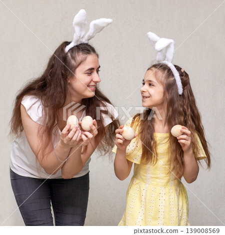 Mother and daughter wearing bunny ears holding wooden eggs and smiling during Easter celebration Mother and daughter wearing bunny ears holding wooden eggs and smiling during Easter celebration 139008569