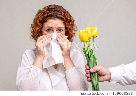 Woman sneezing into tissue after receiving a yellow tulip bouquet showing allergic reaction Woman sneezing into tissue after receiving a yellow tulip bouquet showing allergic reaction 139008598