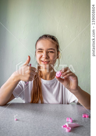 Girl giving thumbs up while winking and holding pink lip balm, enjoying creative self-care moment Girl giving thumbs up while winking and holding pink lip balm, enjoying creative self-care moment 139008604