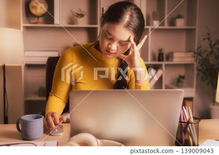 Young Asian woman using laptop and mouse in cozy home office at night, showing focused remote work, online research, concentration, planning, calm evening productivity and digital workflow. Young Asian woman using laptop and mouse in cozy home office at night, showing focused remote work, online research, concentration, planning, calm evening productivity and digital workflow. 139009043
