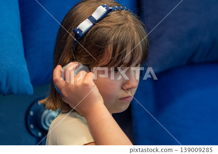 Girl 7 years old holding receiver to ear listening with focus indoors Girl 7 years old holding receiver to ear listening with focus indoors 139009285