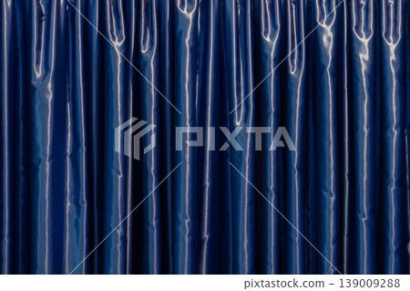 Blue curtain with glossy surface forming vertical folds in interior Blue curtain with glossy surface forming vertical folds in interior 139009288