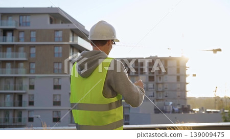 Man constructive engineer with white hard hat and safety vest is using a tablet computer while inspecting a construction site at sunset 139009475