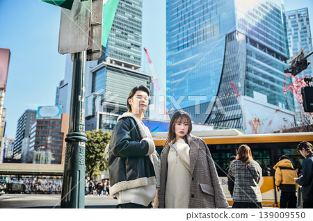 A stylish young couple in winter clothes stands against the backdrop of the Shibuya cityscape. 139009550