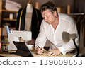 Middle-aged male dressmaker drawing on paper watching video-course 139009653