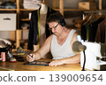 Middle-aged man wearing earphones drawing on tablet in sewing workshop at night 139009654